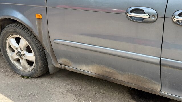 Kia Sedona minivan showing dirty exterior, worn paint, aging body condition and signs of everyday vehicle use on urban street
