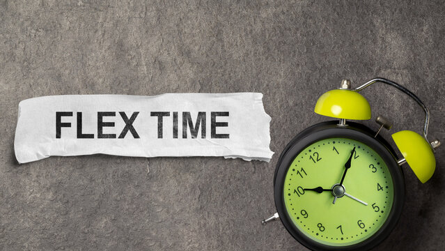 Close-up shot of an analog alarm clock with a neon green face next to a piece of paper with the words FLEX TIME, set against a textured grey background, symbolizing flexible work. Concept of Flextime