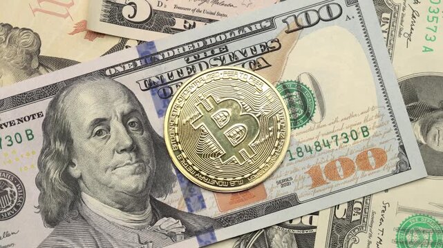 Gold Bitcoin coin lying on US dollar bills, digital currency Bitcoin against the background of the classic hundred dollar bill with Benjamin Franklin.
