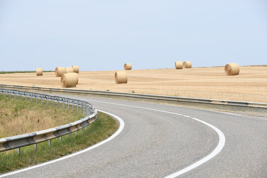 viele Rundballen Stroh nach Getreideernte verteilt auf dem Acker hinter Kurve von Landstra&szlig;e 