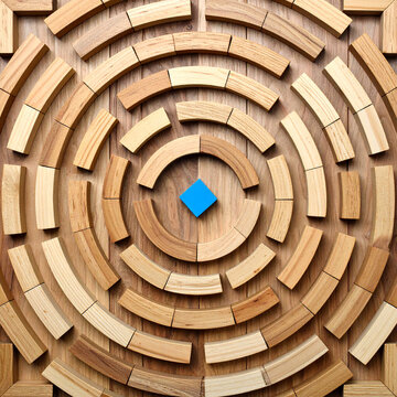 Laberinto circular formado por piezas de madera sobre una superficie de madera, con un elemento azul en el centro. Concepto de estrategia, b&uacute;squeda, objetivo, desaf&iacute;o y resoluci&oacute;n de problemas