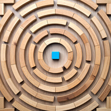 Laberinto circular formado por piezas de madera sobre una superficie de madera, con un elemento azul en el centro. Concepto de estrategia, b&uacute;squeda, objetivo, desaf&iacute;o y resoluci&oacute;n de problemas