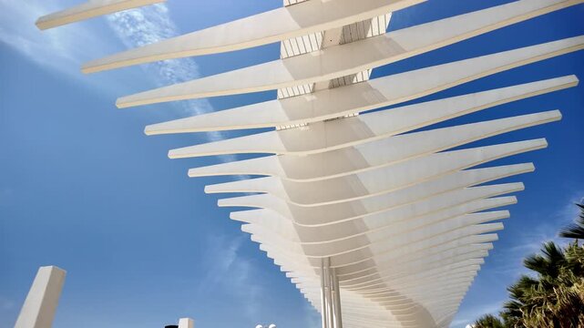 Modern white pergola on the Malaga seafront promenade &ndash; futuristic architecture, blue sky, palm trees and a luxury marina on the Costa del Sol in Spain