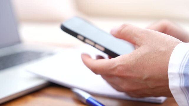 Mobile Phone User Scrolling And Tapping Smartphone With Both Hands Beside Laptop And Notebook, Online Communication, Business Technology, Internet Browsing, Remote Work And Digital Productivity