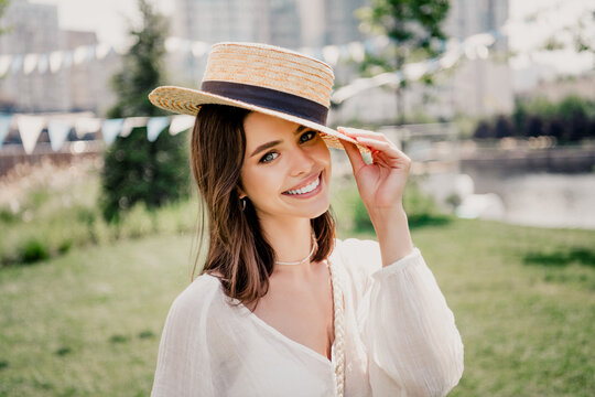 Smiling young woman wearing a straw hat in a sunny outdoor summer portrait with casual white blouse and relaxed, happy mood