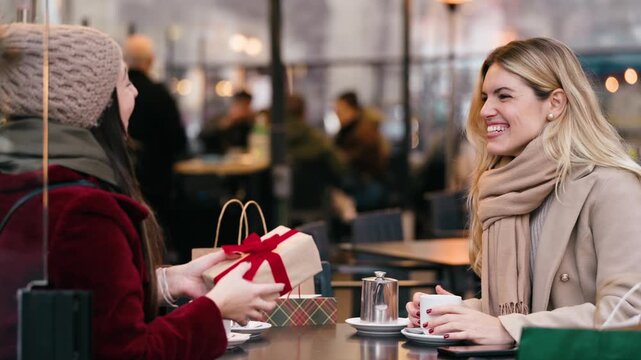 Video of two beautiful friends exchanging Christmas gifts while having a drink on a bar terrace