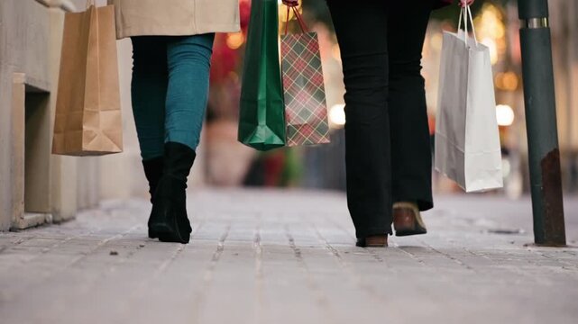 Video of close up of two friends walking on the city street with shopping bags.