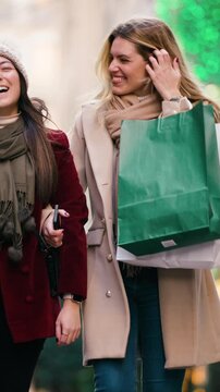 Video of two beautiful friends talking and having fun while walking on the city street with shopping bags.