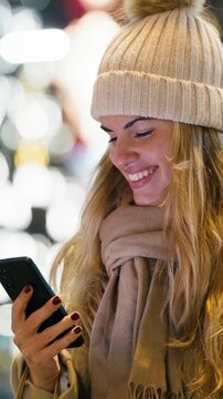 Video of pretty woman using smartphone while walking on the city street in winter with shopping bag.