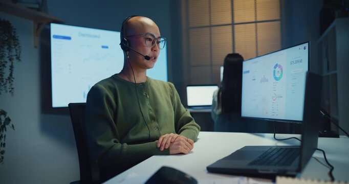 Happy young Asian businesswoman smile looking at camera in call center office at night. Customer service support agent, headset operator representative, online telemarketing work overtime concept.
