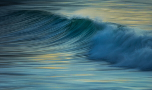Ocean wave at sunrise with spray at the crest at slow shutter speed