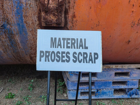 A warning sign indicating scrap material processing placed in front of a rusty industrial metal tank and plastic pallets. Ideal for industrial safety documentation, recycling concepts, manufacturing 