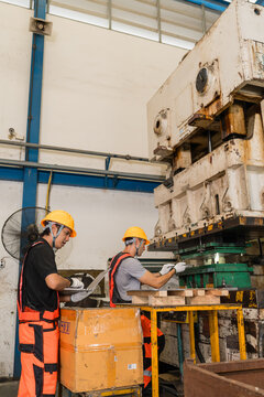 Workers with laptop and sheet metal panel beside rusty industrial punch press