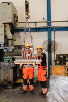 Factory workers guiding suspended chain hoist load beside old power press machine