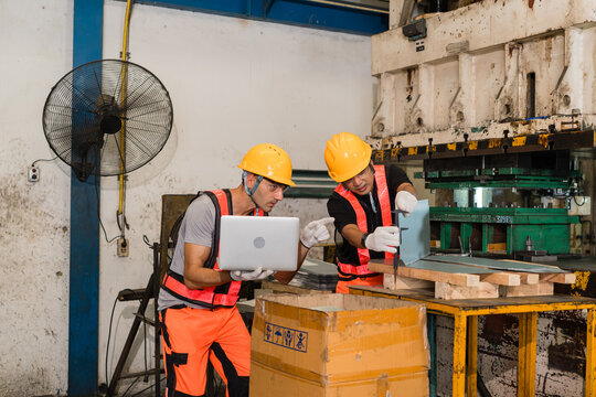 Engineer pointing at laptop screen as colleague measures metal bracket with calipers