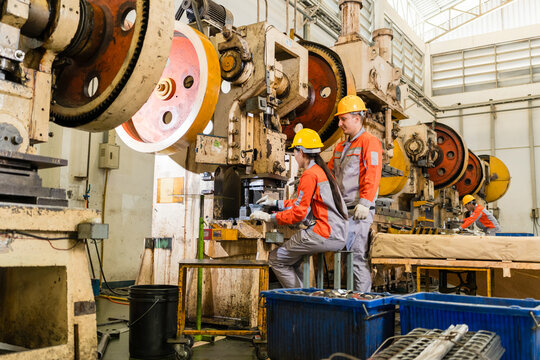 Two machine operators collaborating at power press station along a row of stamping machines supporting efficient production and workplace safety inside a busy metalworking factory setting