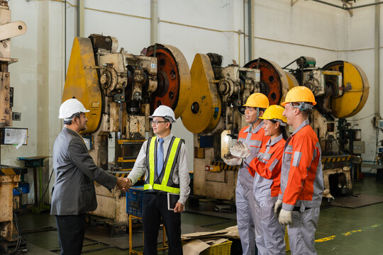 Two engineers shake hands while three workers clap beside mechanical stamping press machines with visible flywheels on the factory floor