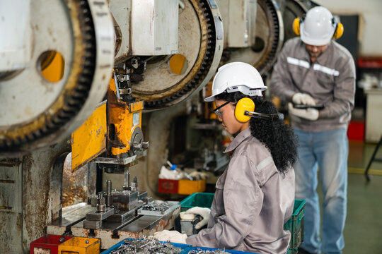 Woman machine operator sorting stamped metal parts beside mechanical punch press in factory