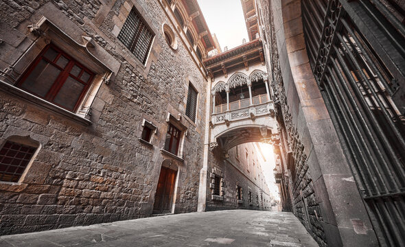 Barcelona, Spain. Barri Gotic Quarter. Antique Bridge between stone walls of medieval buildings in in old town. Famous touristic landmark and travel destination. Sunset evening street perspective.