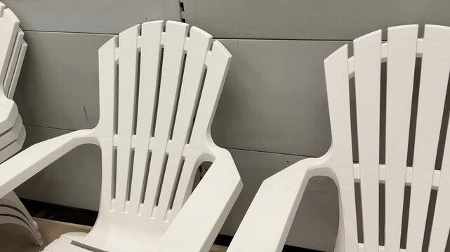 Identical white plastic chairs are lined up in a home and garden department, presenting a clean and organized display of practical outdoor furniture for seasonal use. Close up.