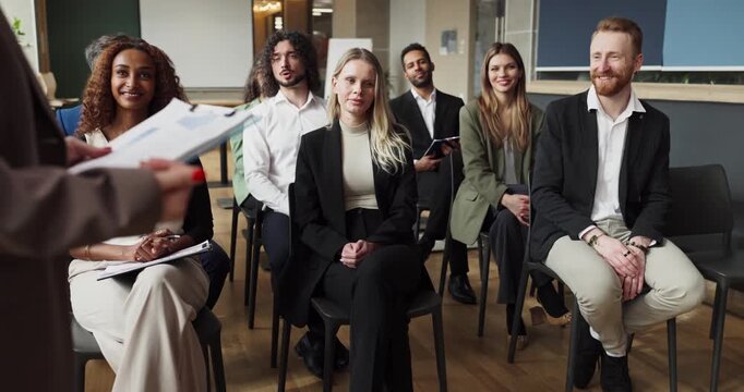 Team listens to speaker while employees participate. In a modern office, a coach leads a diverse audience, guiding seminar discussion. Concept shows teamwork and steady training progress.