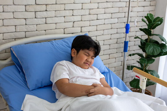 A sick boy lies in a hospital bed, one hand clutching his stomach, resting during treatment and recovery. This relates to healthcare, child care, illness, fever, patient care, and hospitals.