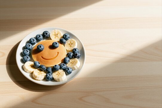 smiling pancake breakfast with bananas and blueberries on a sunny wooden table