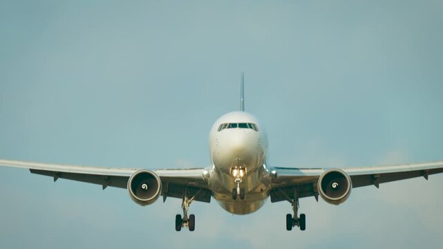 Jet engine close up. Passenger airplane approaching runway with symmetrical front perspective and blue sky background. Global aviation fleet airport arrivals and long haul transportation