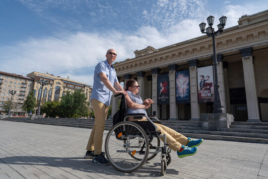 paralyzed female disabled person in a wheelchair on a walk around the city, accompanied by her husband's assistant