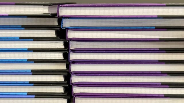 Thick notebooks in assorted colors are arranged in organized stacks at a retail display, providing practical stationery choices for school, office tasks, note taking and creative writing. Close up.