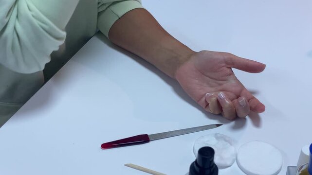 A woman's open hand rests palm-up on a white table after filing her nails. She pauses during her manicure routine with calm satisfaction. This peaceful self-care moment feels gentle and serene.
