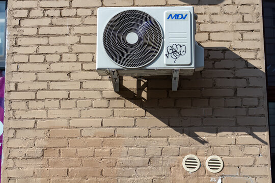 White external air conditioning unit installed on a brown brick wall in urban environment
