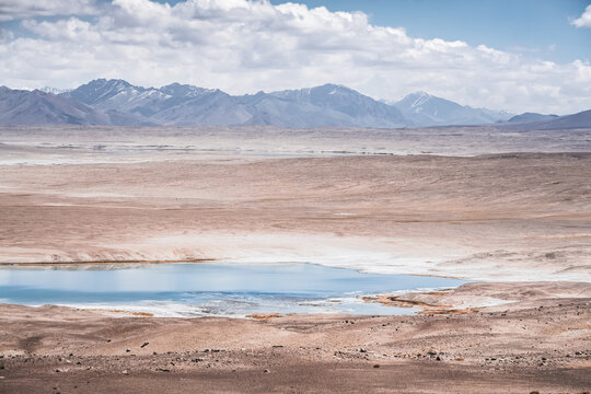 Panorama of a mountain landscape with a lake and river with clear water on a plateau in the Tien Shan Mountains in the Pamirs, mountain ridges and slopes with snow in the background