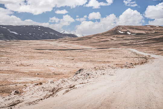 Dusty road of the Pamir Highway winds and twists in the valley of the Tien Shan mountains in Tajikistan in Pamir, landscape in the high desert mountains for background