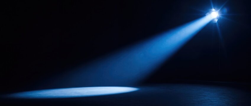 Bright blue spotlight casting dramatic illumination across dark empty stage performance floor
