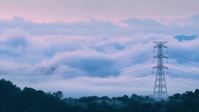 A high voltage electricity pylon stands amidst rolling clouds and fog over a lush green forest at sunrise in Xindian, New Taipei City, Taiwan.