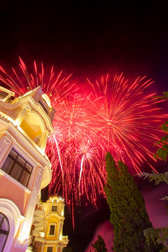 Brilliant red fireworks exploding above illuminated historic architecture during a festive night celebration. Colorful fireworks display over an elegant building against the dark night sky with copy s