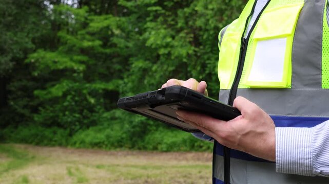 Close-up of a forestry engineer or environmental specialist using a digital tablet app to collect, analyze, and enter ecological data outdoors in a dense forest area. Environmental  inspection.