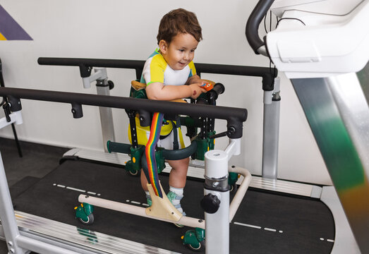 Handsome young boy with movement disorders is satisfied with his rehabilitation exercises using a walker on a treadmill. Children's disability and rehabilitation