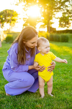 a mother teaches her child to walk on the green grass of a lawn, a mother and child having fun together in the summer, first steps
