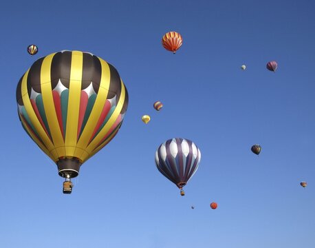 Multiple colorful hot air balloons floating in clear blue sky with balloons