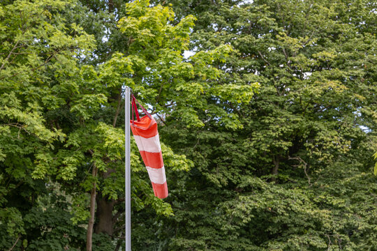 Orange and white windsock on metal pole against green trees on a summer day