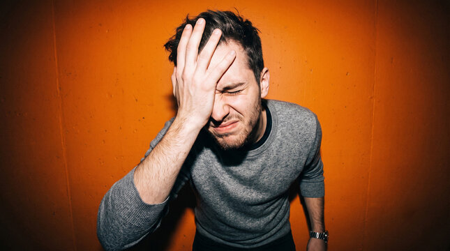 Young Caucasian man doing facepalm gesture on orange background