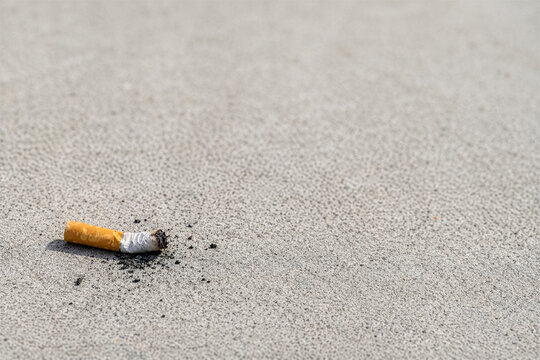 Cigarette butt and ash littering a concrete ground. Representing pollution, addiction, no smoking and public health issues with copy space