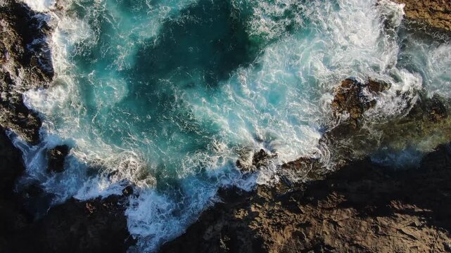 Beautiful top down aerial view of turquoise ocean waves crashing against the rugged volcanic coast of Gran Canaria, Canary Islands, Spain