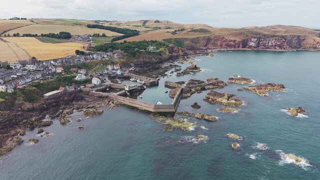 Scenic semi-circular pan left to right over St Abbs fishing harbour and coastal village, showcasing the dramatic rocky shore and North Sea coastline in Berwickshire, Scotland