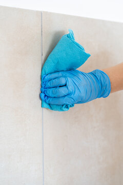 Close-up of person in blue nitrile glove wiping ceramic wall tiles with a microfiber cloth. Professional cleaning service or home maintenance concept.