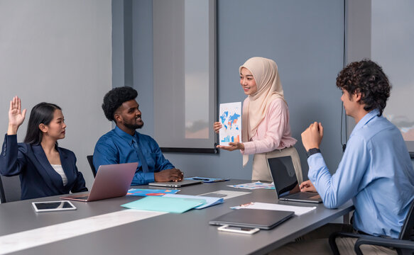 asian businesswoman in hijab presenting a chart report to multiracial team,a colleague raising hand,asking questions and collaborating on a project in meeting room