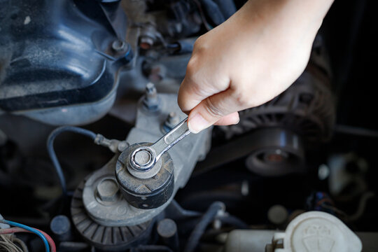 Hand of mechanic using a silver combination wrench to work on a pulley bolt