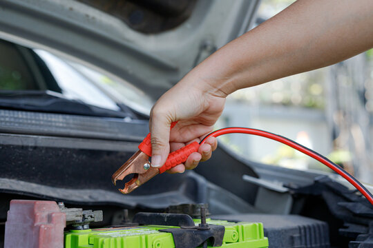 Hand holding jumper cable clamp near car battery